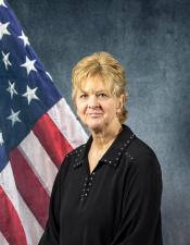 Portrait of Katheryn Schroeder sitting in front of an American flag