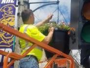 A person on orange scaffolding hanging a planter filled with flowers from a lamp post 
