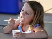 A young girl sitting at a table eating vanilla ice cream