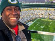 RV Jedeye in a Green Bay Packers beanie at Lambeau Field with an aerial view of the field behind