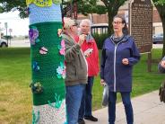 Yarn art adorning lamp post with three artisits talking in background.