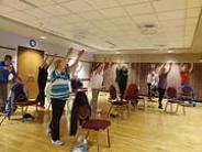 People standing next to chairs with their arms raised, doing chair yoga