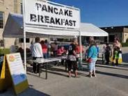 People lined up at tent with sign that reads "Pancake Breakfast"