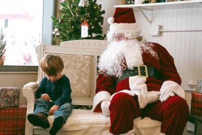 Little boy sits on small sofa next to Santa.
