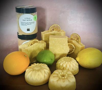 Various soaps and one jar of citrus scrub pictured along with a couple of lemons and a lime.