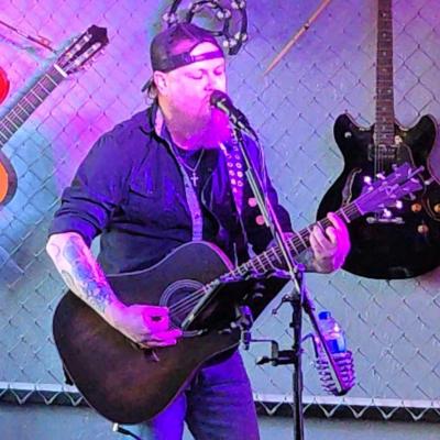 Man singing and playing guitar onstage.