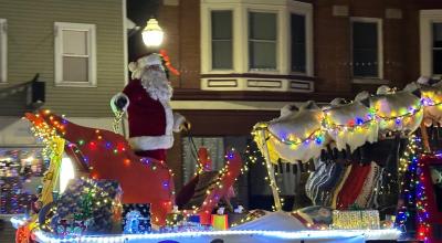 Santa standing next to his sled on a decorated parade float.
