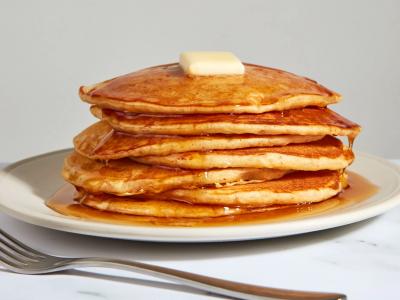 A white plate holding a stack of buttered pancakes.