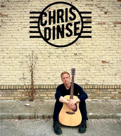 Man sitting against a brick wall and holding a guitar.