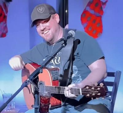Smiling man in ball cap playing guitar onstage.