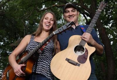Smiling man and woman standing outdoors and holding guitars.