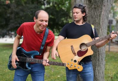 Two smiling men outdoors holding guitars.