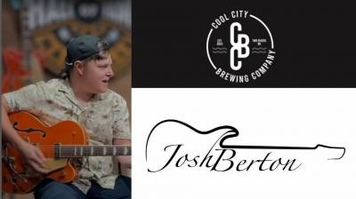 Man with backward ballcap sitting onstage playing guitar and singing.