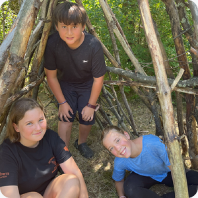 Three happy kids inside a makeshift natural structure.
