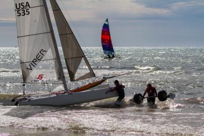 Catamaran and crew in foreground with colorful sail in background.