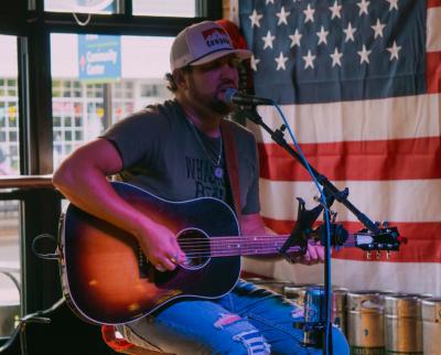 Bearded man in ballcap playing guitar and singing onstage.