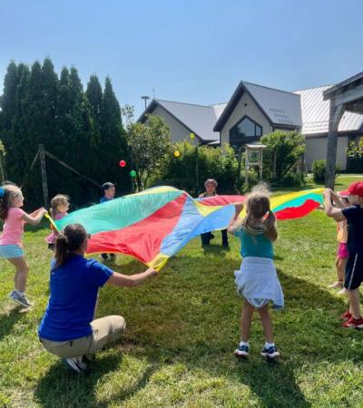 Adult and children grasp a parachute and bounce balls atop it.