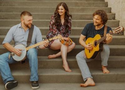Man with banjo on left, woman with tamborine in center, and man with guitar on right, all sitting on steps.