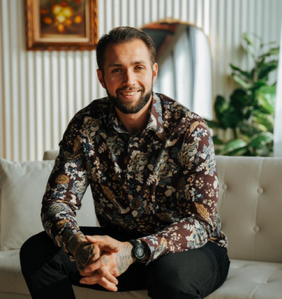 A seated, smiing bearded man.