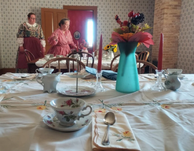 Two ladies in historical dress in background with a nicely-set table in foreground.