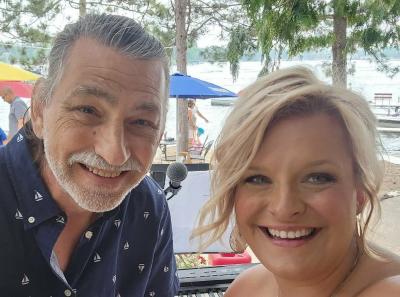 Smiling man and woman with beach umbrellas, beach and water in the background.