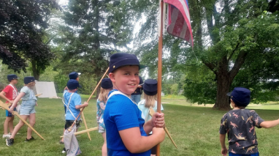 Boy in cap holding a flag with other kids moving in background.