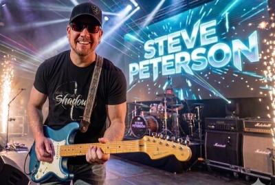 Smiling man with ballcap and sunglasses playing guitar onstage.