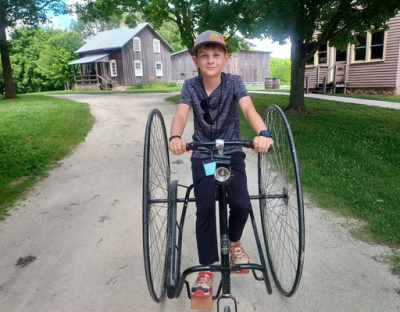 Boy in ballcap riding an old-fashioned bike down a path.
