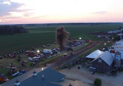 Truck on a dirt track emitting dark smoke as it pulls heavy weight.