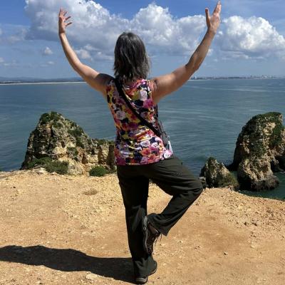 Woman holding a yoga pose on sandy ledge overlooking a body of water.