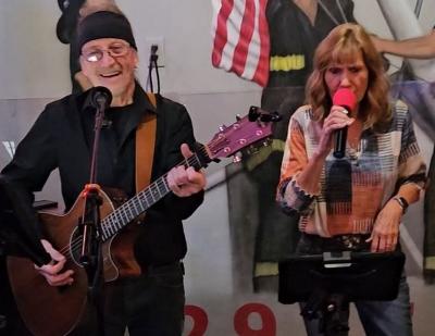 Man with guitar and singing woman perform onstage.