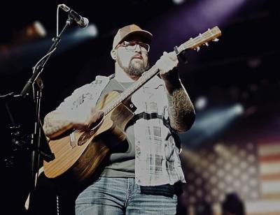 Man in ballcap playing guitar onstage.