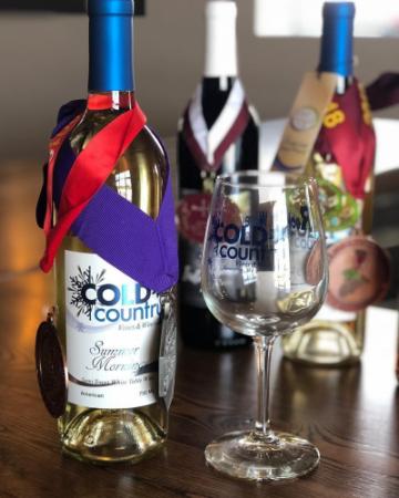 Three bottles of wine with award medals hanging from them, plus a Cold Country wine glass.