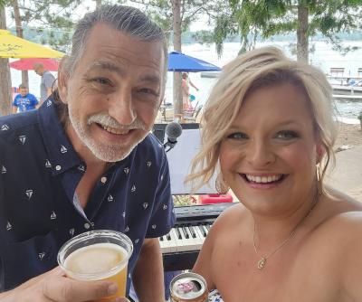 Smiling man and woman with keyboard, beach umbrellas, beach and water in the background.