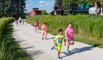 Several childern running down a path with an old train in the background.