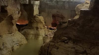 A well-lit cave with water and rough cave pillars.