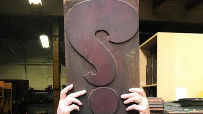 Pair of hands holding a large piece of wood type with a question mark.