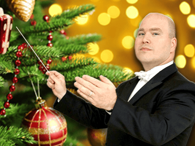 Man conducting, with twinkle lights and Christmas tree in background.