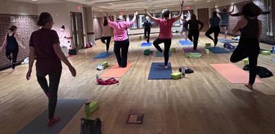 Folks holding yoga pose standing on yoga mats.