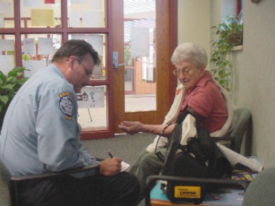 Woman seated in chair wearing a blood pressure cuff. Paramedic takes her blood pressure