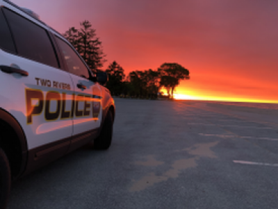 White police car driving into the sunset. Text on car reads "Two Rivers Police"