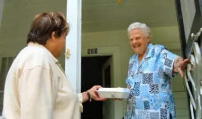 Woman handing a box of food to a senior woman who is holding the door open.