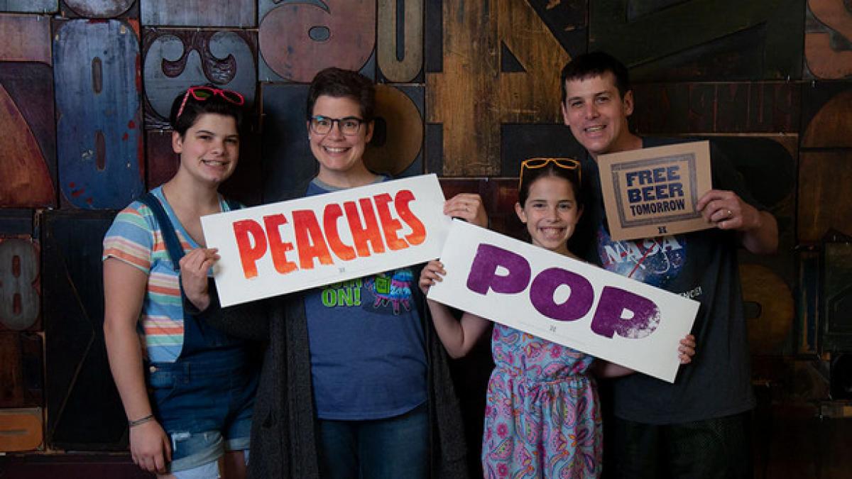 Four people holding signs that say Peaches, Pop, Free beer tomorrow