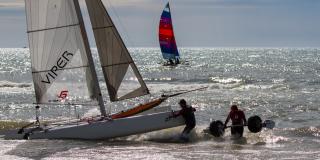 Catamaran and crew in foreground with colorful sail in background.