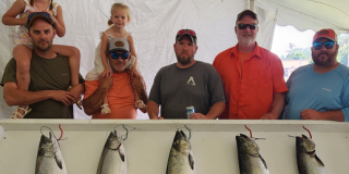 Five men (two with little girls upon their shoulders) stand behind fish caught in derby.