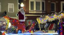 Santa standing next to his sled on a decorated parade float.