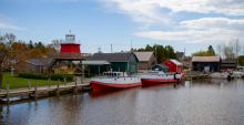 A view of Rogers Street Fishing Village with two red and white boats docked at a wooden dock next to a small red lighthouse.