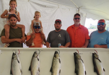 Five men (two with little girls upon their shoulders) stand behind fish caught in derby.