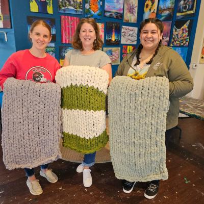 Three women holding chunky blankets.