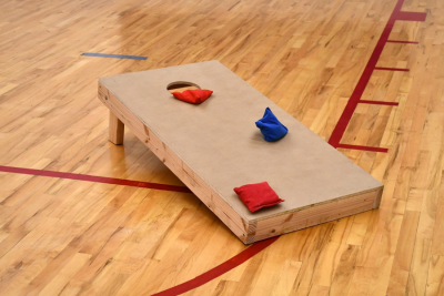 Cornhold board with three bean bags on a gym floor.